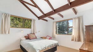 Ein Schlafzimmer mit einem Bett, zwei Fenstern, einer Holzbalkendecke und einem Nachttisch.
