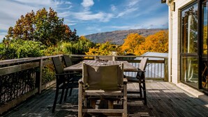 Eine Holzdielen-Terrasse mit Tisch und Stühlen, mit Blick auf eine schöne Aussicht auf Bäume und Berge.