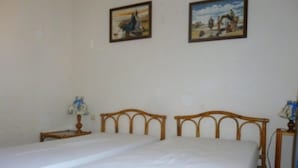 A room with two single beds, a small bedside table with a lamp, and two framed pictures on the wall.