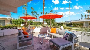 An outdoor patio area with seating arrangements, including sofas and chairs, and two red umbrellas providing shade. - A Design-Forward Midcentury Residence in Central Palm Springs! (Palm Springs)