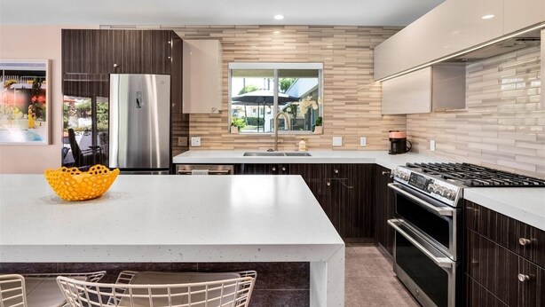 A modern kitchen with a central island, stainless steel appliances, and a view to the outdoors. - A Design-Forward Midcentury Residence in Central Palm Springs! (Palm Springs)