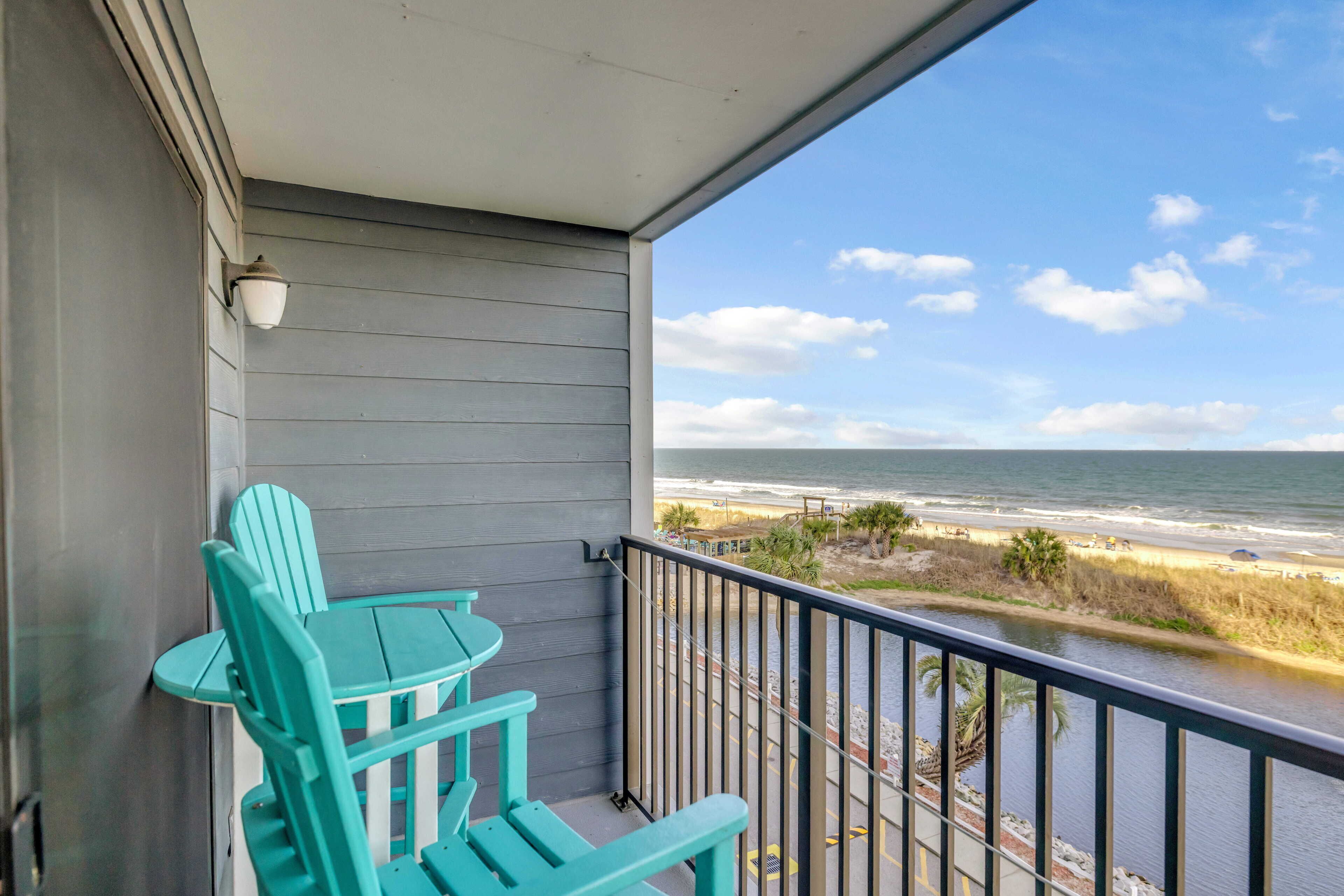 A balcony with turquoise chairs and a view of the beach.