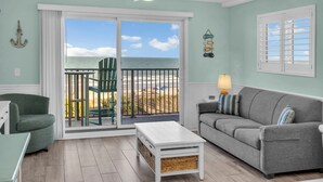 A room with a balcony, a green chair, a grey sofa, a white coffee table, and a lamp. - Direct OCEANFRONT 3rd floor End unit Myrtle Beach Resort (Myrtle Beach)