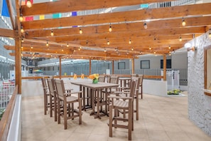 Une terrasse extérieure avec des tables et des chaises en bois, des guirlandes lumineuses et une vue sur le paysage urbain.