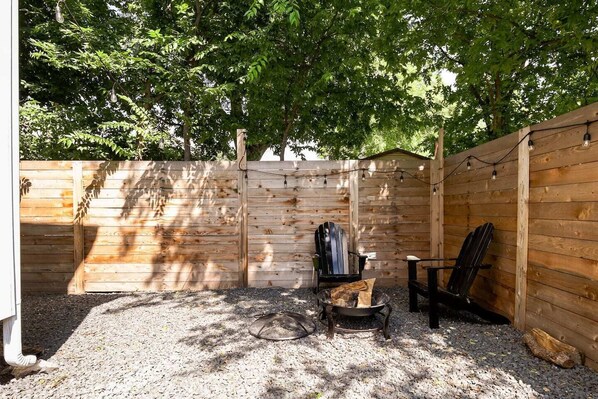 A wooden deck with a metal fire pit, two Adirondack chairs, and a wooden fence. - Eastside Escape *backyard games, Walk to Bars, Brews & Good Eats* (Austin)
