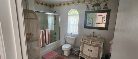 Een badkamer met een douchecabine van glas, een toilet, een wastafel met decor kastje en een spiegel met bloemenversiering.