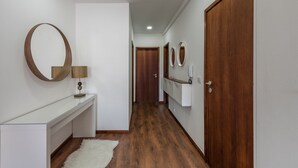 Un couloir doté d’un plancher en bois, de murs blancs et d’une console blanche sur laquelle se trouve une lampe. On y trouve deux portes en bois et un miroir accroché au mur.