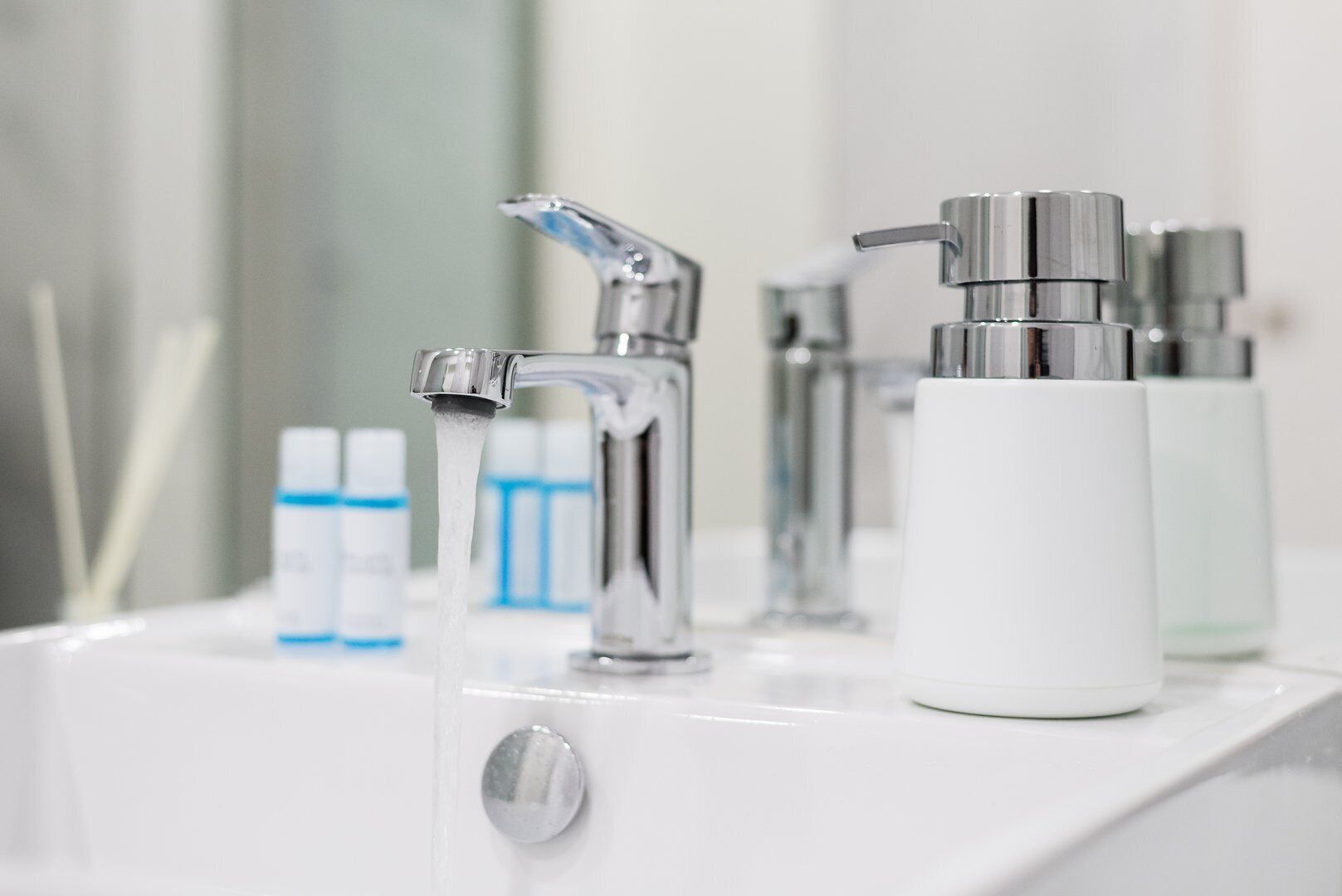 A bathroom sink with a modern faucet and a white bottle of hand soap.