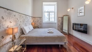 Une chambre à coucher avec un lit, des lampes de chevet, une télévision, une fenêtre et un miroir.