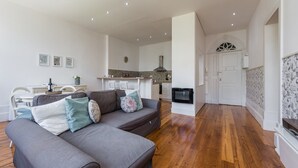 Un salon moderne avec un canapé gris, un parquet en bois et une cuisine en arrière-plan.