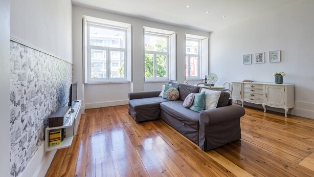 Un salon spacieux doté d’un plancher en bois, d’un canapé gris, d’une armoire blanche et de grandes fenêtres.