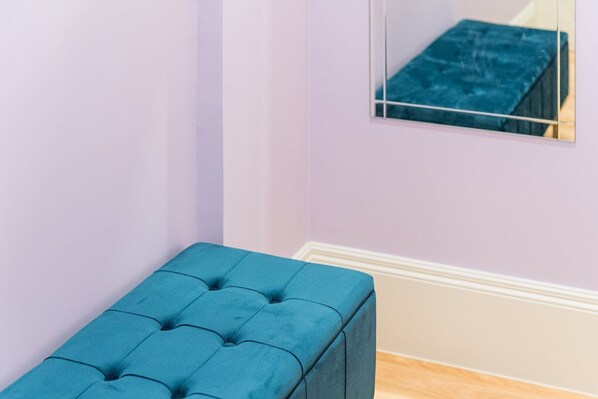 A corner of a room with a teal upholstered bench and a mirror reflecting a blue upholstered bench.