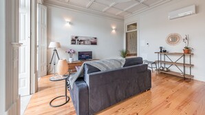 Ein modernes Wohnzimmer mit grauem Sofa, Holzboden, Fernseher und dekorativem Spiegel.