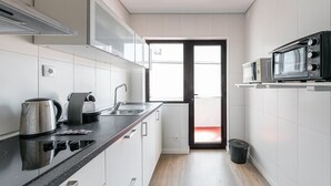 Una cocina moderna con armarios blancos, encimera negra, hervidor de acero inoxidable, cafetera, microondas y una ventana con una puerta roja.