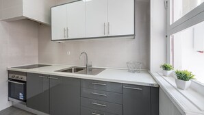 A modern kitchen with a double sink, dark cabinets, and a window with potted plants. - GuestReady - October Tide (Porto)