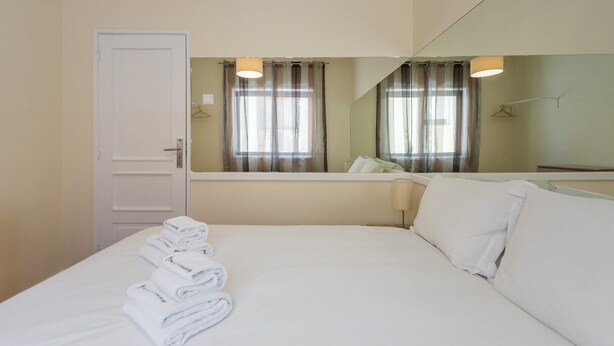 A hotel room with a bed, a mirror, a window with curtains, and a door. - GuestReady - October Tide (Porto)