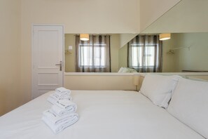 Une chambre d’hôtel avec un lit, un miroir, une fenêtre avec des rideaux et une porte.