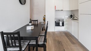 A modern kitchen with white cabinets, a built-in oven, and a dining area with a black table and chairs. - GuestReady - Cosy spot near Porto city centre (Porto)
