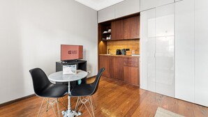 A compact hotel room with a small dining area featuring a round table and two chairs, a kitchenette with wooden cabinets, and a flat-screen TV on a stand. - GuestReady - Rivoli Studio (Porto)