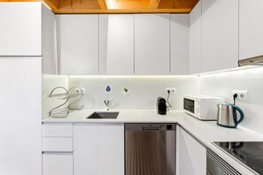 Eine moderne Küche mit weißen Schränken, einer Edelstahl-Spüle, einem Wasserkocher, einer Mikrowelle und einem Geschirrspüler.