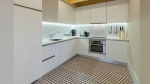 A modern kitchen with white cabinets, a patterned floor, and wooden ceiling beams. - GuestReady - Cottage core in Marques (Porto)