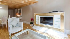 A modern living room with a white sofa, a glass coffee table, and a fireplace with a TV. - GuestReady - Cottage core in Marques (Porto)
