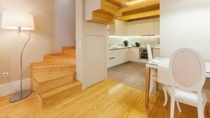 A modern kitchen with white cabinets, a wooden staircase, and a dining area with a white chair. - GuestReady - Cottage core in Marques (Porto)