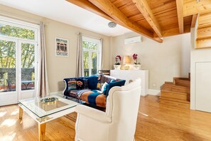A living room with a sofa, a glass coffee table, a white armchair, a white cabinet with decorative items, and a staircase.
