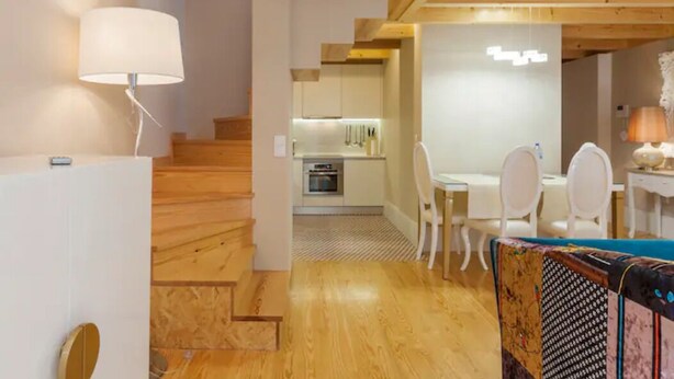 A modern interior with wooden floors, a staircase, a dining area with white chairs, and a kitchen with white cabinets. - GuestReady - Cottage core in Marques (Porto)