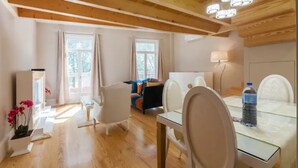 A spacious living area with wooden beams, a dining table with chairs, a sofa, and a window with curtains. - GuestReady - Cottage core in Marques (Porto)