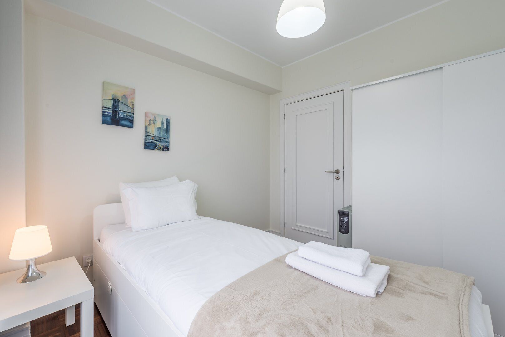 A neatly made bed with white linens, a bedside lamp, and a folded towel on the bed.
