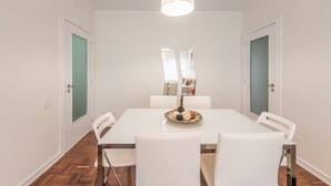 A dining area with a white table, white chairs, a hanging light fixture, and a mirror on the wall.