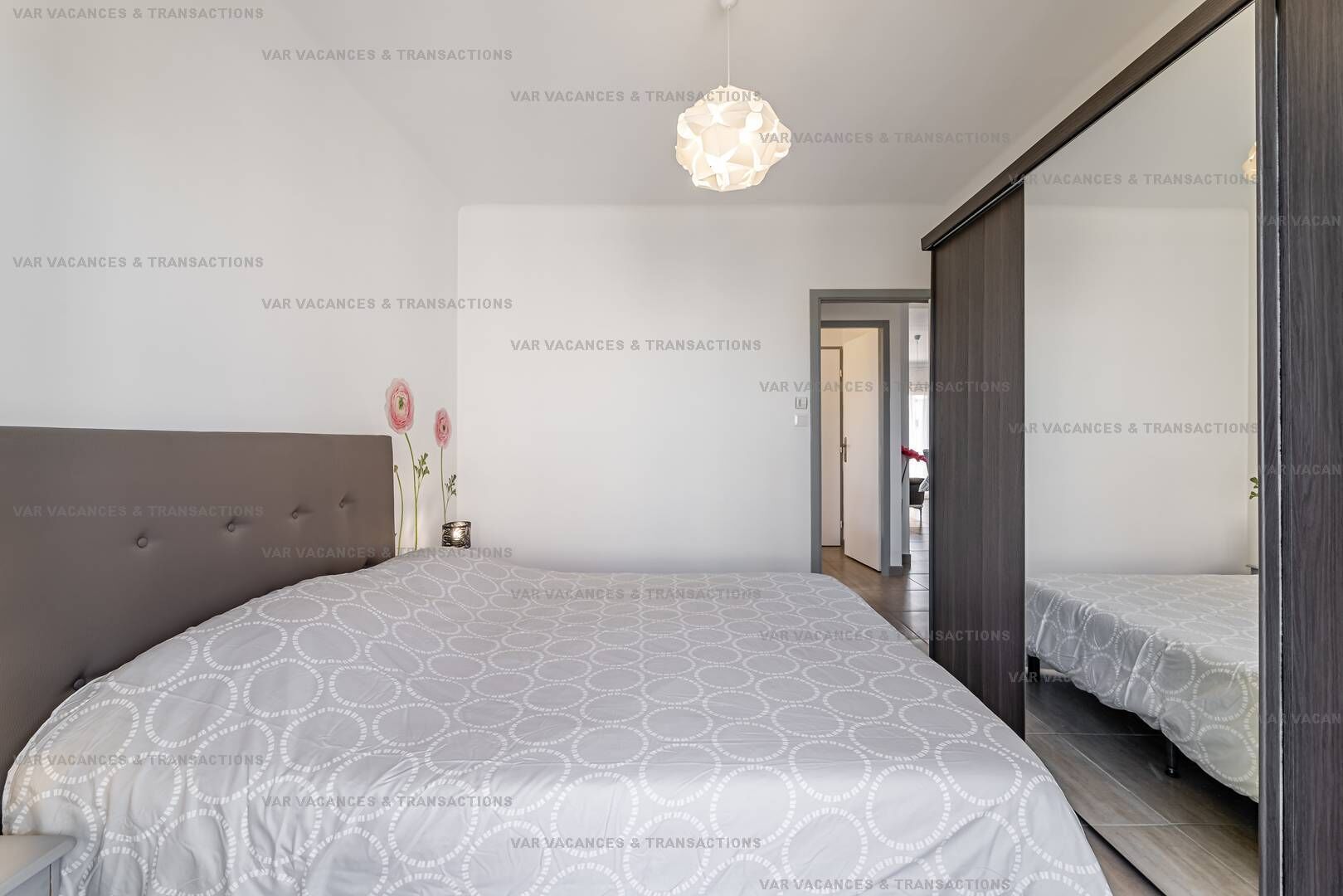 A modern bedroom with a grey tufted headboard, a patterned bedspread, and a hanging light fixture.