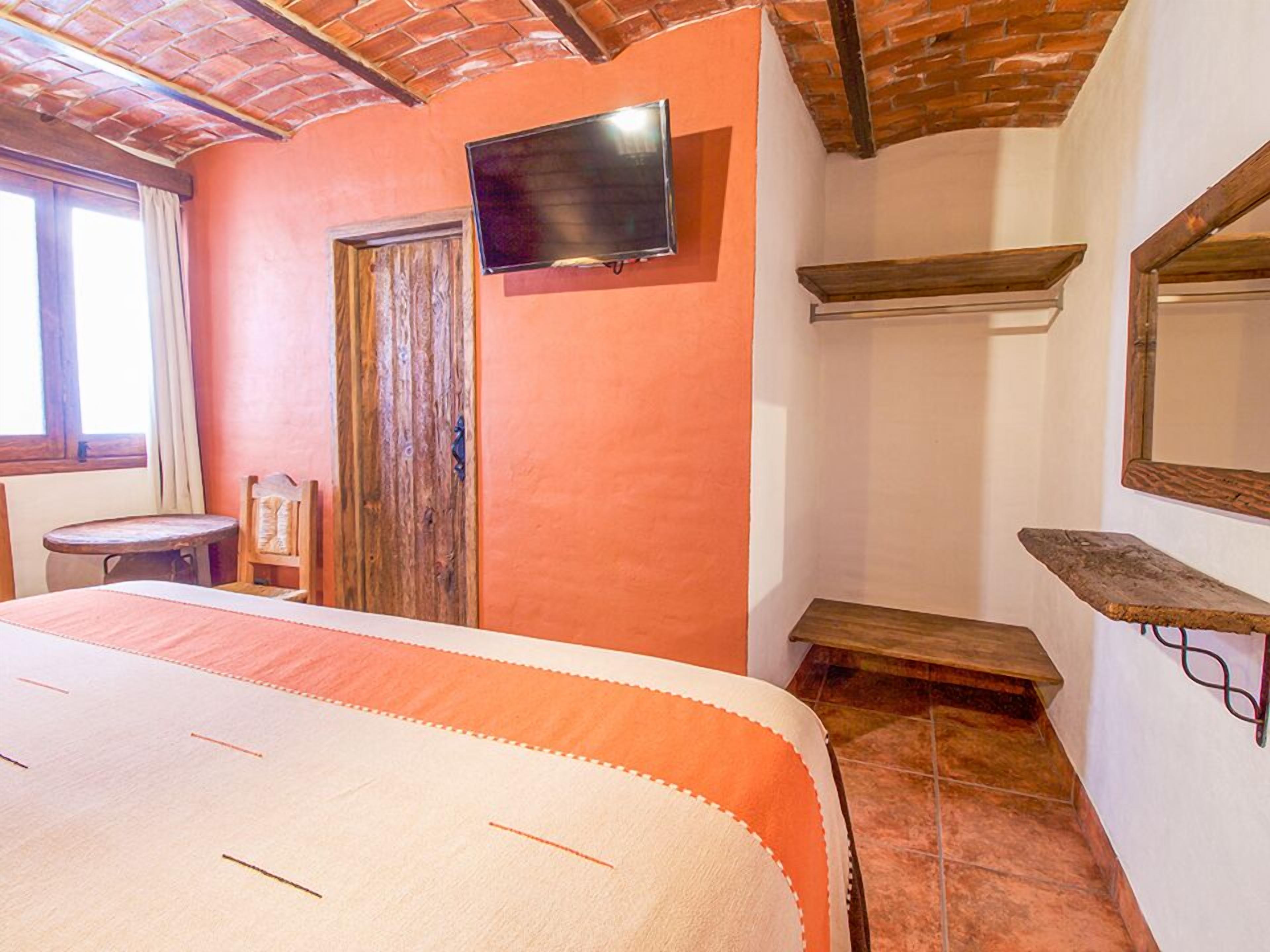 A bedroom with a bed, a TV mounted on the wall, a wooden door, and a window.