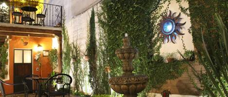 An outdoor patio with a stone fountain, outdoor seating, and a sun-shaped wall decoration.