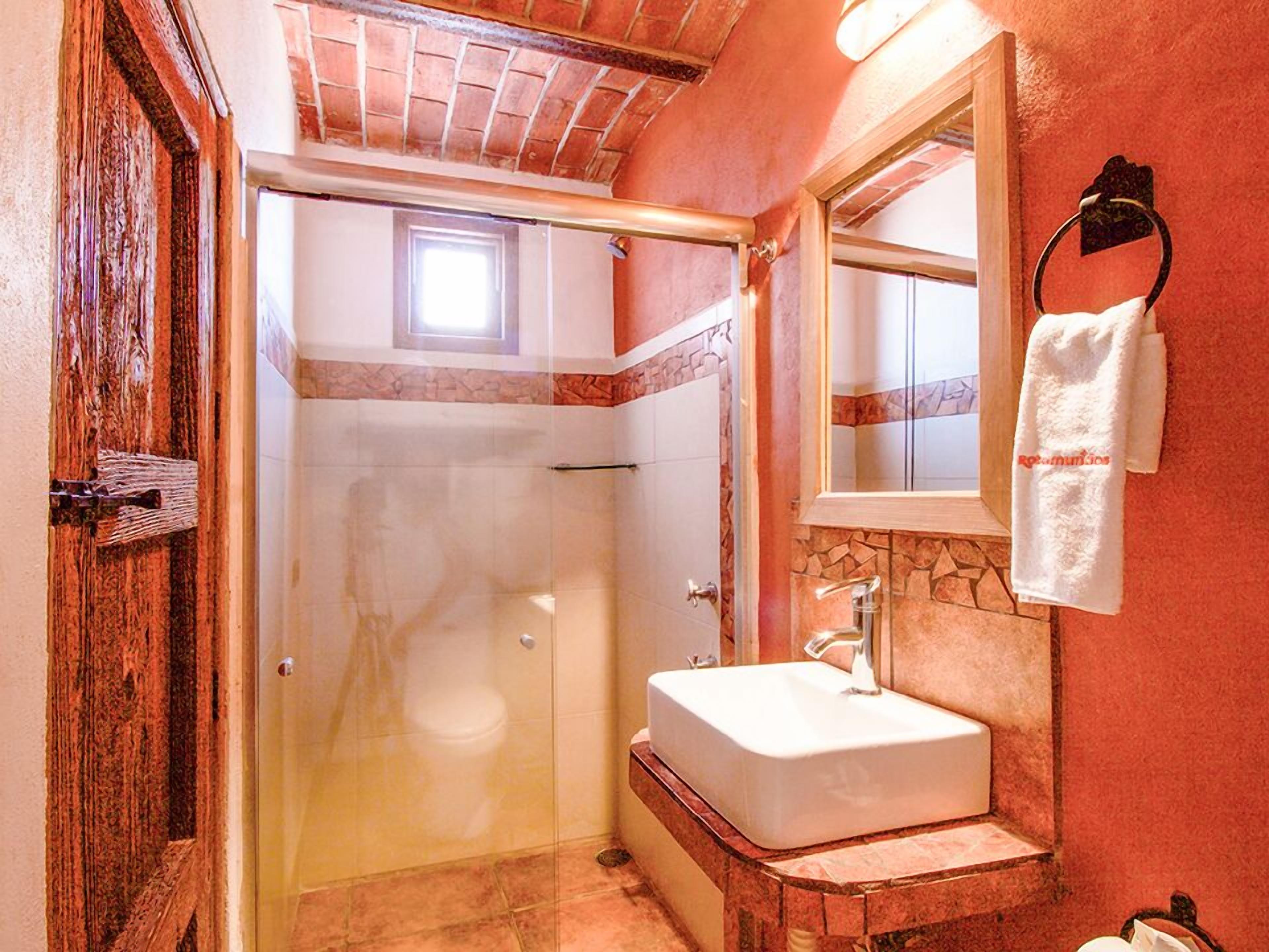 Un baño con cabina de ducha de vidrio, un lavamanos blanco y un espejo encima.