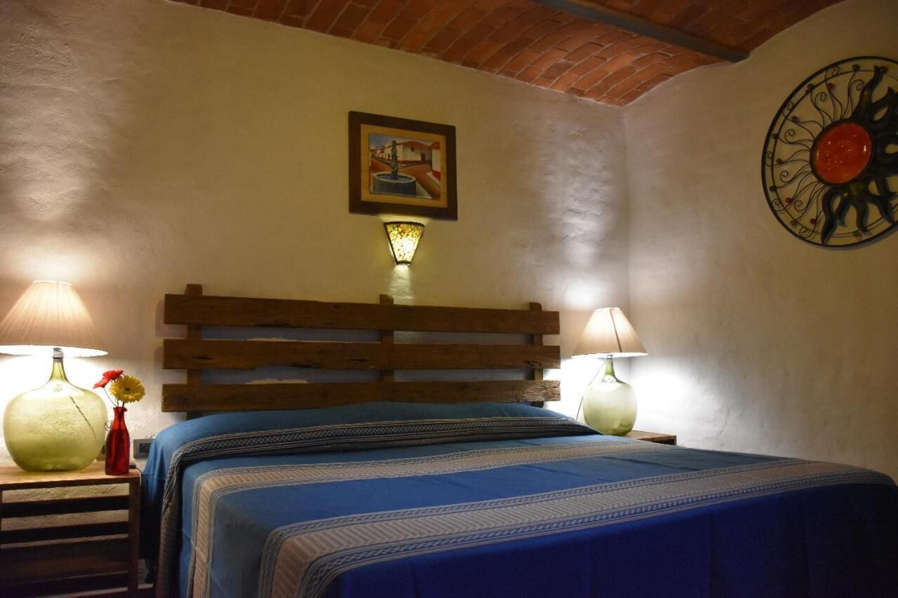 A bedroom with a wooden headboard, two bedside lamps, a framed picture on the wall, and a decorative wall piece.