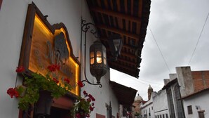 A narrow street with a building featuring a sign with a clock and a hanging flower basket. -  Hotel Mi Pueblito Tapalpa (Tapalpa)