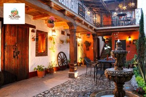Un patio tradicional con piso de piedra, puertas de madera y una fuente.