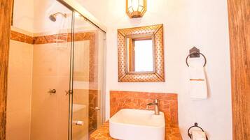 A bathroom with a glass shower enclosure, a sink with a marble countertop, a wall-mounted mirror, and a towel rack with a towel.