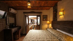 A bedroom with a wooden ceiling, a bed with patterned bedding, a desk with a chair, a wall-mounted air conditioner, and a staircase leading to an outdoor area. -  Hotel Mi Pueblito Tapalpa (Tapalpa)