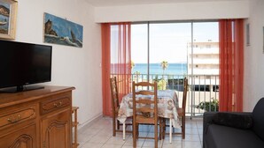 En balkon med et bord og stole, et fjernsyn på et træskab og udsigt til havet.