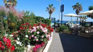En sti kantet med farverige blomster, der fører til et siddeområde med parasoller, med udsigt over en strand.