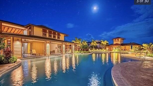 Zona de piscina nocturna con vista clara a la piscina, edificios circundantes y una luna visible en el cielo.