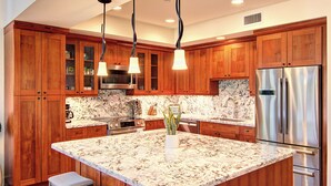 Una cocina con armarios de madera, un refrigerador de acero inoxidable, una isla de mármol e iluminación colgante.