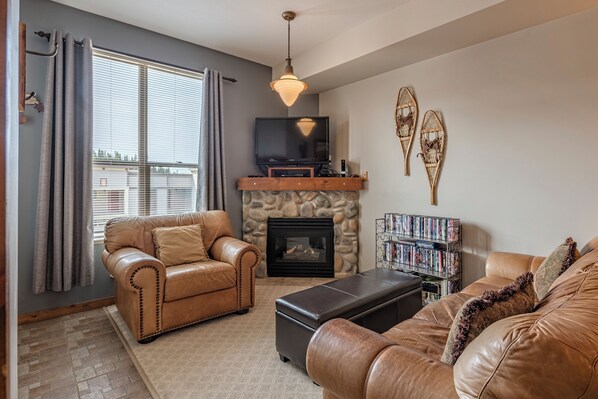 A living room with leather sofas, a stone fireplace, a television, and a bookshelf.