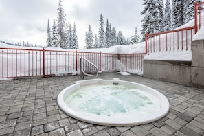 Un bain à remous installé dans un espace extérieur enneigé, avec une clôture rouge et des arbres couverts de neige en arrière-plan.