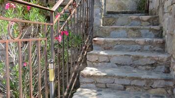 A stone staircase with a metal railing, leading to a building with a tiled roof and a window with a shutter.