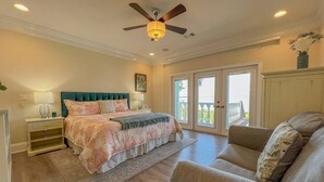 Ein Schlafzimmer mit Bett, Nachttisch, Stuhl, Deckenventilator und Blick ins Freie durch eine Schiebetür.