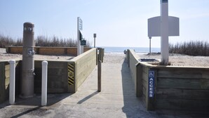Ein Holzsteg führt zu einem Strand mit einem Sandweg und hölzernen Geländern.